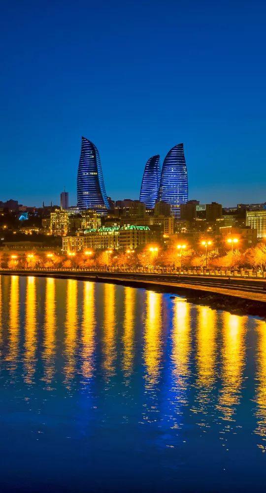 Cityscape of Baku, Azerbaijan at twilight featuring the illuminated Flame Towers and historical buildings in the foreground