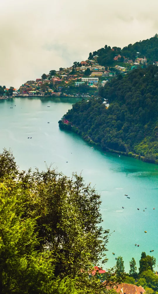 Aerial view of Naini Lake in Nainital, surrounded by lush green hills and colorful buildings